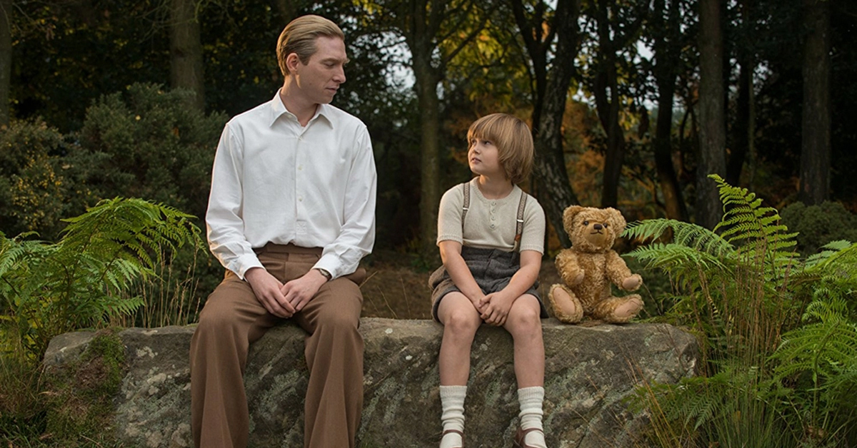 domhnall gleeson and will tilston sitting on a rock in a forest with a teddy bear