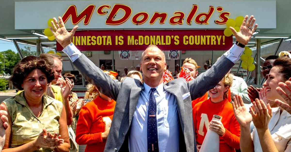 michael keaton holding his arms up in a crowd in front of a mcdonald's