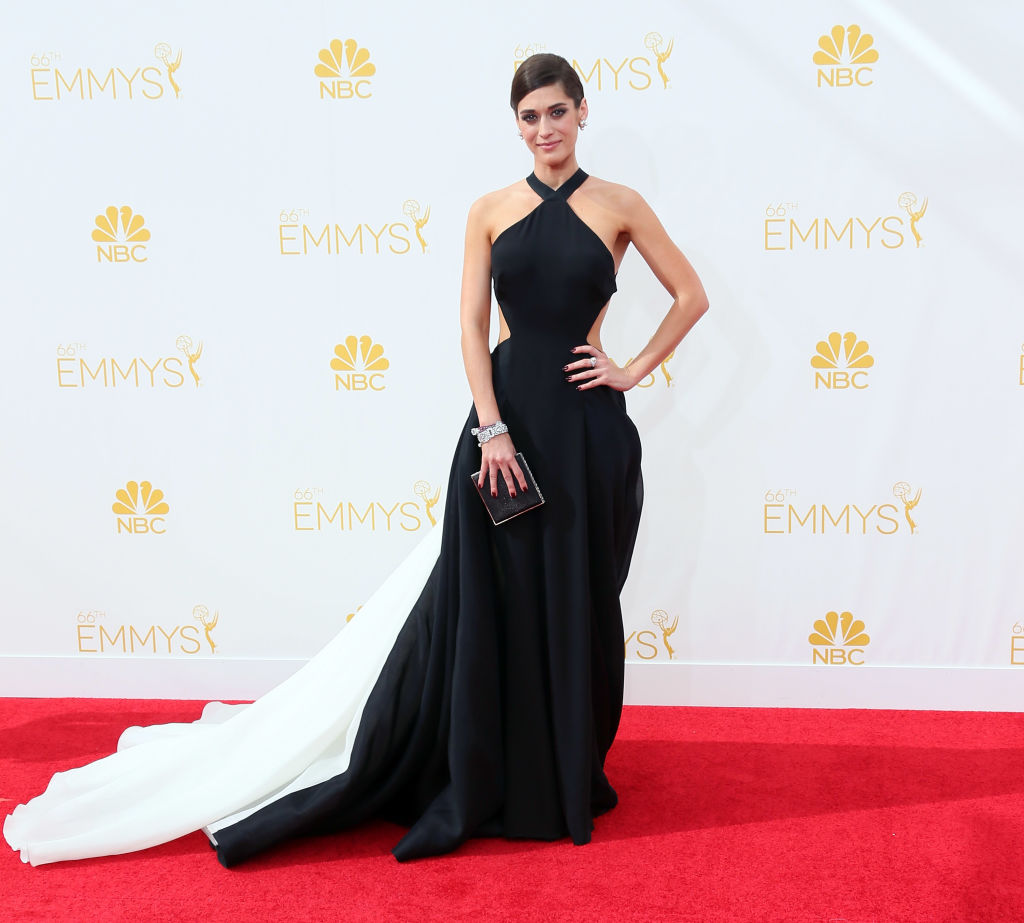 Lizzy Caplan wears a black gown with a white train.