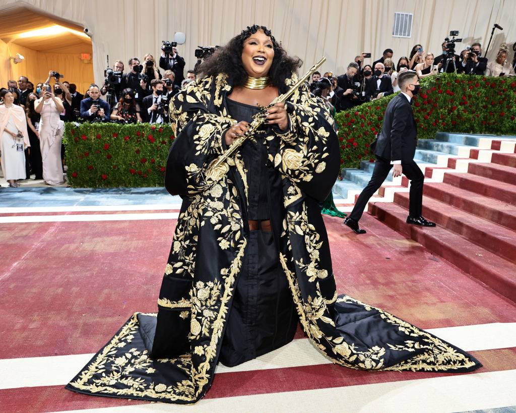 lizzo in a black and gold gown with a flute